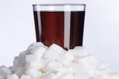 Glass of sugar and sugar cube on white background